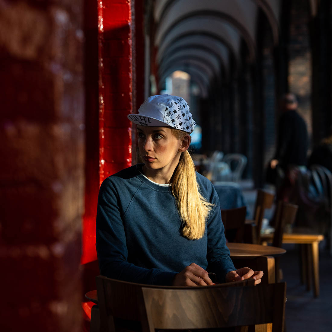 kobieta siedzi przy stoliku w oczekiwaniu na kawę i ma na głowie białą czapkę Luxa Coffee Ride